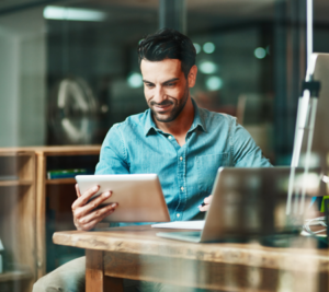 Un jeune homme assis dans un bureau en train de regarder quelque chose sur sa tablette dans le but d'entreprendre.