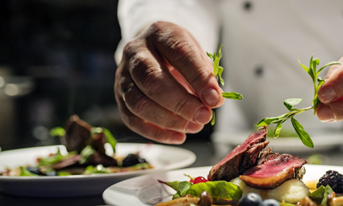 Main d'un chef dressant une assiette gastronomique