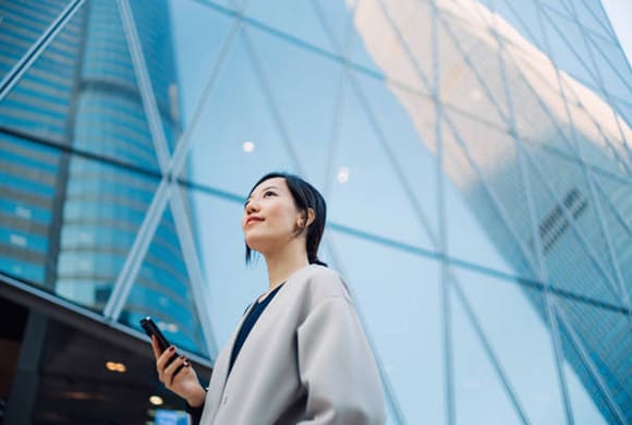 femme devant un building qui regarde vers le ciel en souriant