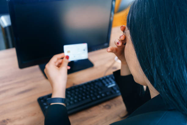Femme attristée et tenant sa carte bancaire dans ses mains face à un ordinateur