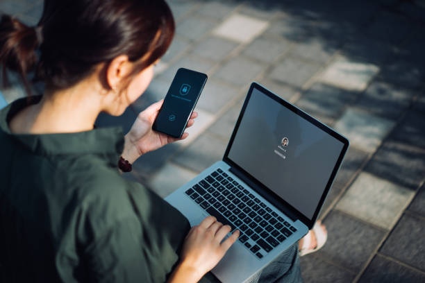 Femme assise dans un parc avec son ordinateur sur les genoux et son téléphone dans les mains avec un écran de connexion de sécurité