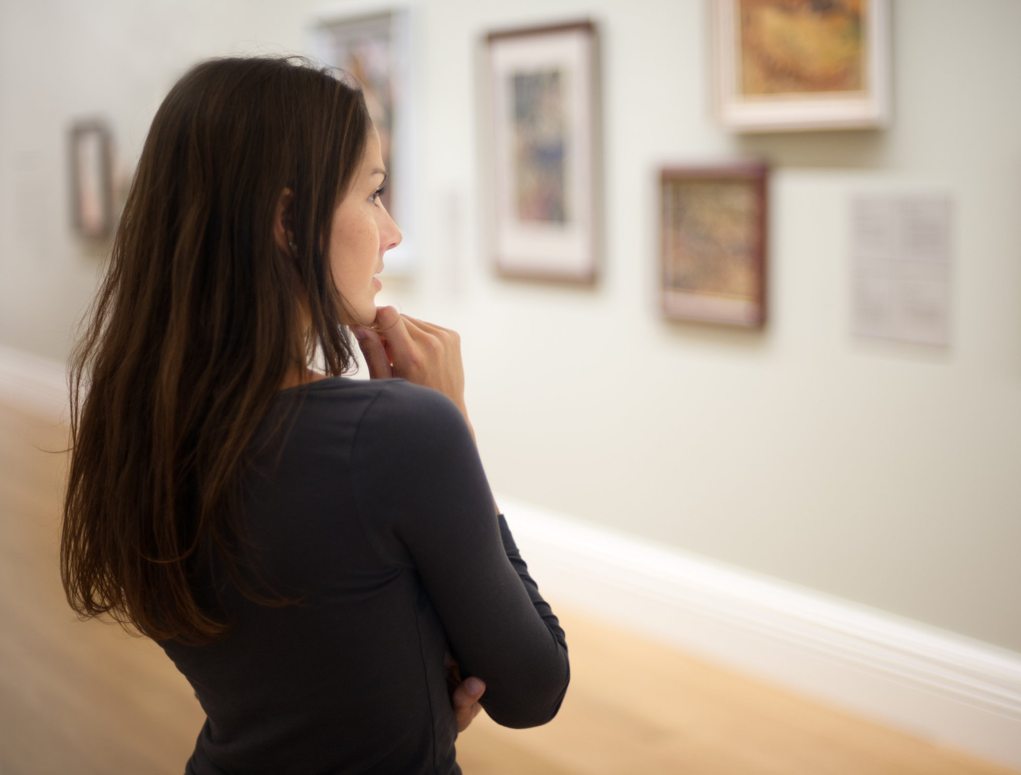 Une jeune femme aux cheveux bruns observe attentivement les tableaux d'un musée, plongée dans un moment de contemplation artistique.